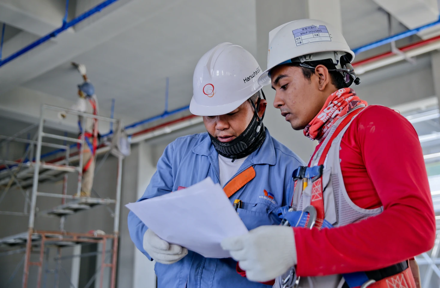 Two men in hard hats and gloves looking at a paper.