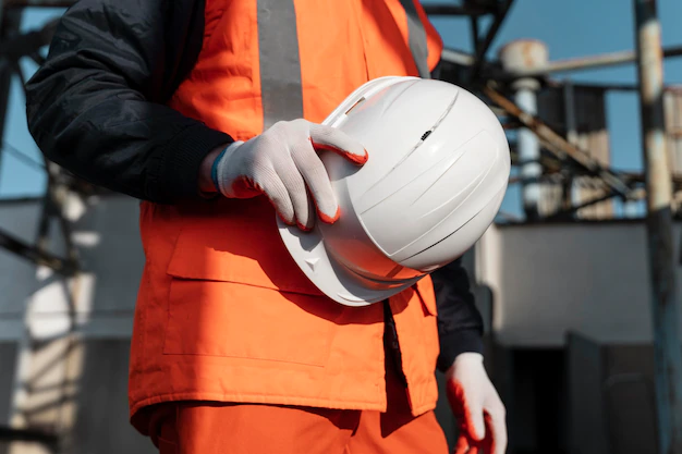 A man in an orange vest holding a white helmet.